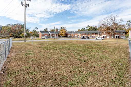 A large grassy field with a fence and a building in the background.