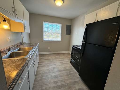 A black refrigerator is in a kitchen with a window.