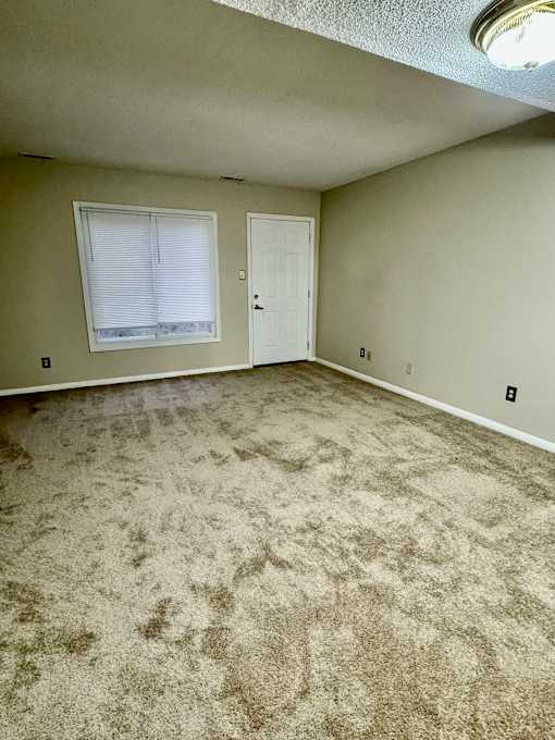 A room with a carpeted floor and a window with blinds.