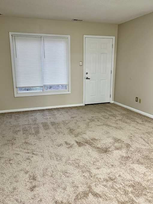 A room with a carpeted floor, a door, and a window with blinds.