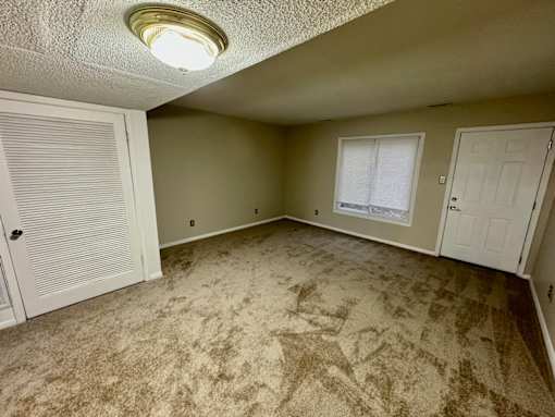 A room with a carpeted floor and a window with blinds.