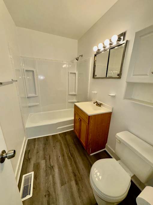 A white bathroom with wood flooring and a white toilet.