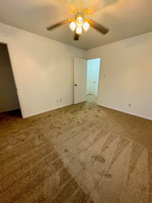 A room with a carpeted floor and a ceiling fan.