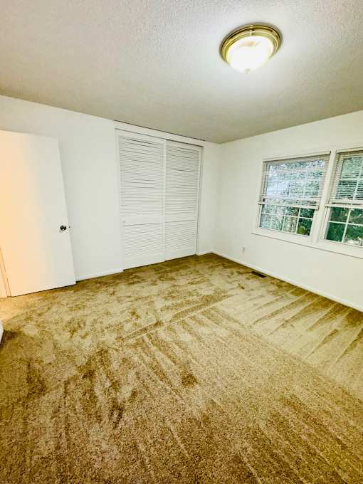A room with a carpeted floor and a window with blinds.