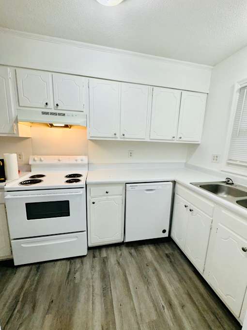 A white kitchen with wood flooring and white appliances.