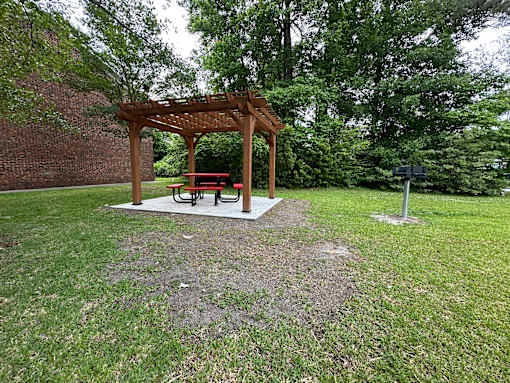 A wooden pergola with a bench is situated in a grassy area.