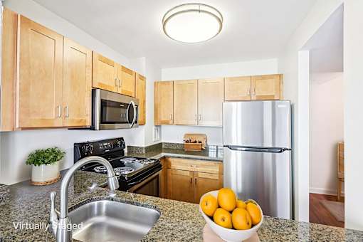 A kitchen with a stove, microwave, refrigerator, and a bowl of oranges on the counter.