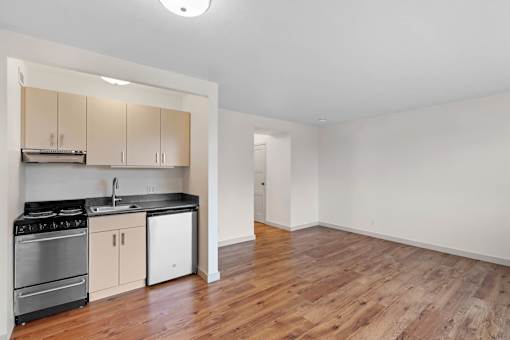 an empty living room with a kitchen with a stove and refrigerator