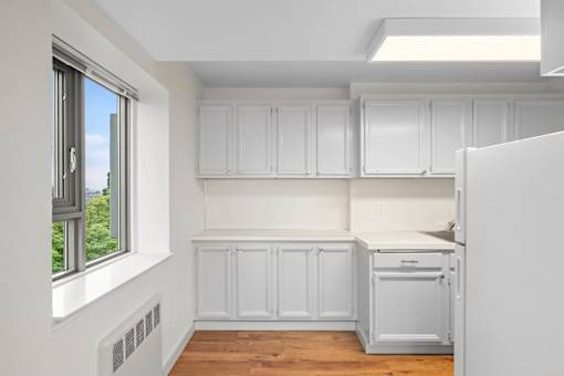 an empty kitchen with white cabinets and a window