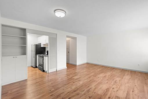 an empty living room with wood flooring and a kitchen