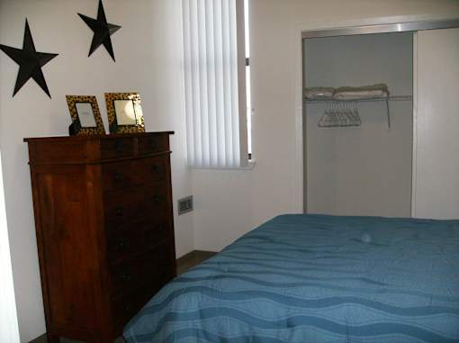 A bedroom with a blue bedspread and a wooden dresser.