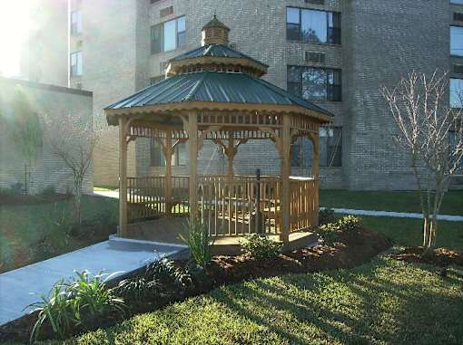 A gazebo is surrounded by a small garden and a pool.