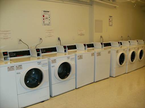 A row of white front load washing machines are lined up in a laundromat.