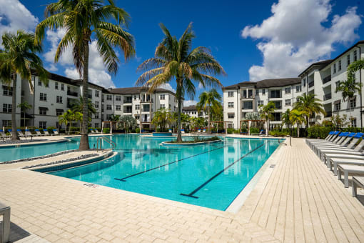 a large swimming pool with palm trees in front of apartment buildings