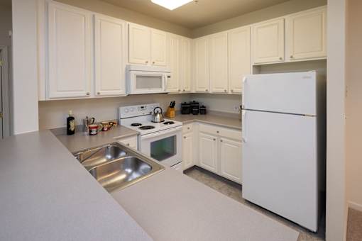 A white kitchen with a refrigerator, sink, stove, and microwave.