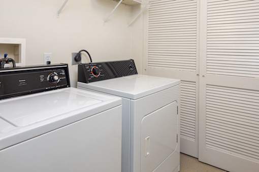 A black and white washing machine sits next to a white dryer in a laundry room.