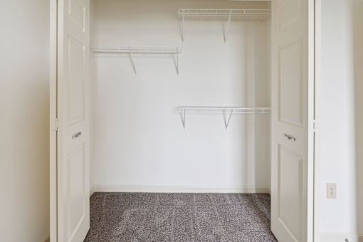 A white closet with two shelves and a grey carpet.