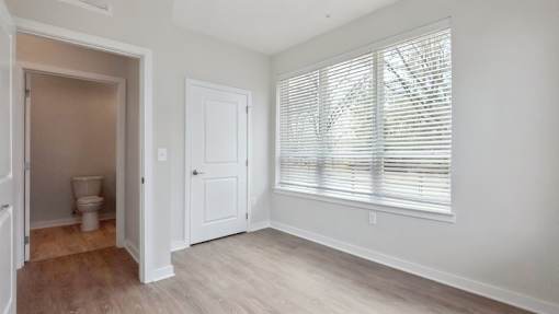 A room with a toilet, a door, and a window with blinds.