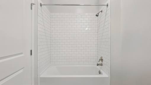 A white bathroom with a white tub and white tiles.