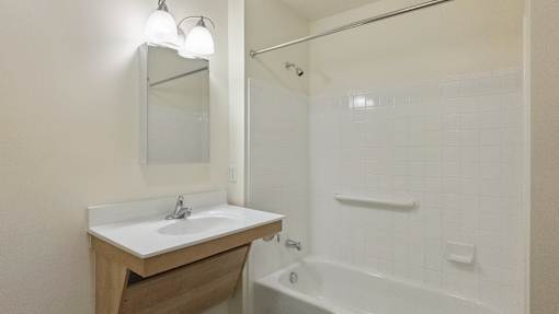 A white bathroom with a sink, mirror, and bathtub.