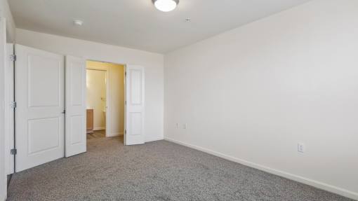 A room with white walls and carpeted floor with two doors open.
