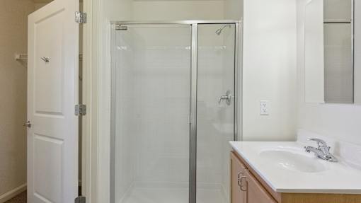 A white bathroom with a sink, mirror, and shower.
