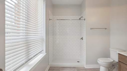 A white bathroom with a toilet, sink, and a shower with a white tile wall.