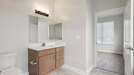 A bathroom with a white toilet, a sink with a wooden cabinet and a mirror above it.