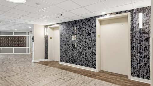 A hallway with a patterned wallpaper and a wooden floor.