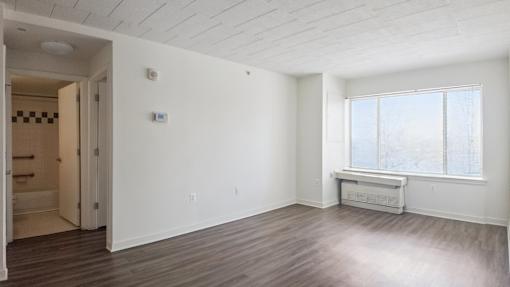 A large empty room with a window and a door leading to a bathroom.
