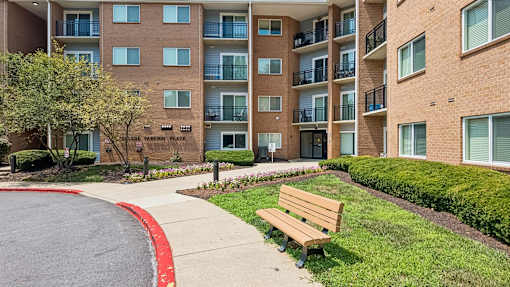 A large apartment complex with a red curb and a bench in front.