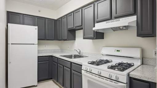 A white refrigerator sits in a kitchen with dark grey cabinets.