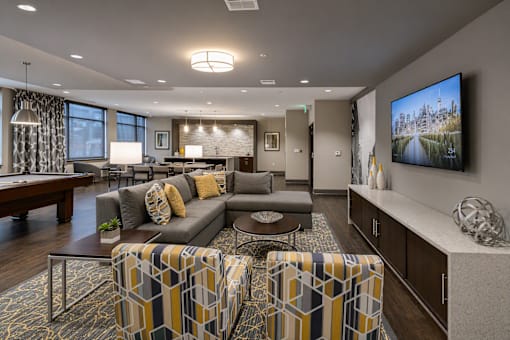 A modern living room with a grey couch, a coffee table, and a large TV on the wall.