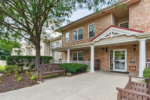 A brick house with a porch and a tree in front.