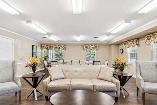 A living room with a beige sofa, two chairs, and two tables with vases of flowers.