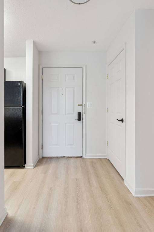 A black refrigerator sits next to a white door in a room with wooden floors.