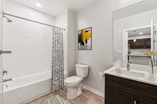 A bathroom with a white toilet, a shower with a black and white curtain, and a painting on the wall.