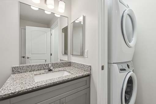 A modern bathroom with a granite countertop and a washer and dryer built into the wall.