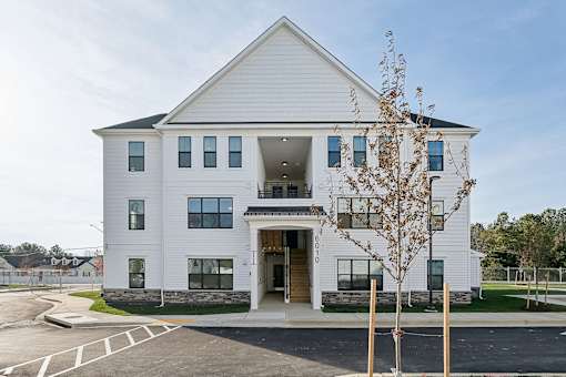 A white two-story building with a black roof and a parking lot in front.