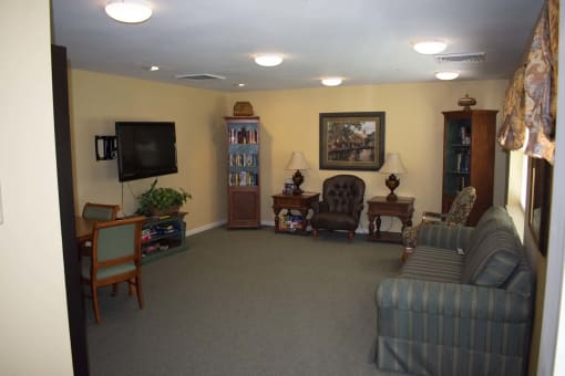 Community room with bookshelves, couch, chairs, and a television.
