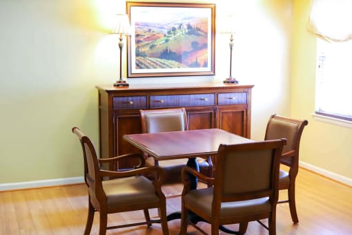 A community room table with four chairs and a painting on the wall.