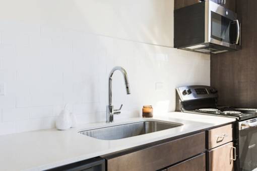 A modern kitchen with a stainless steel sink and a microwave above the stove.