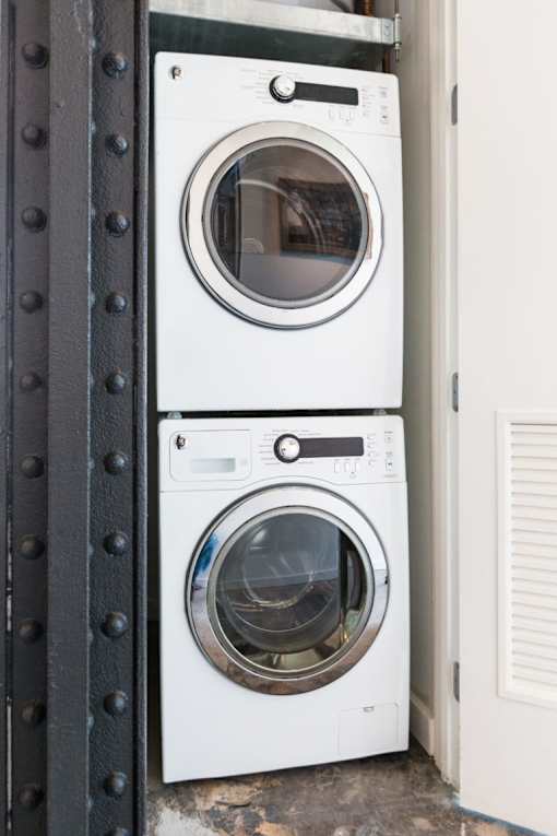 Two white front loading washing machines stacked on top of each other.
