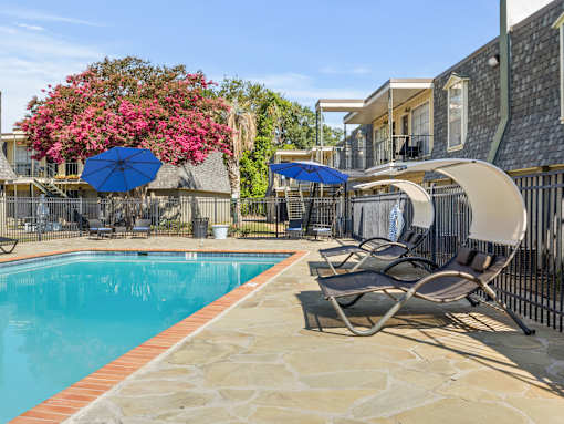 A pool surrounded by chairs and umbrellas with a building in the background.