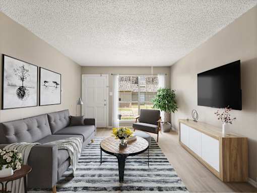 A living room with a grey couch, a coffee table, a chair, a plant, and a flat screen TV mounted on the wall.