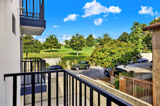 A balcony overlooks a parking lot and green trees.