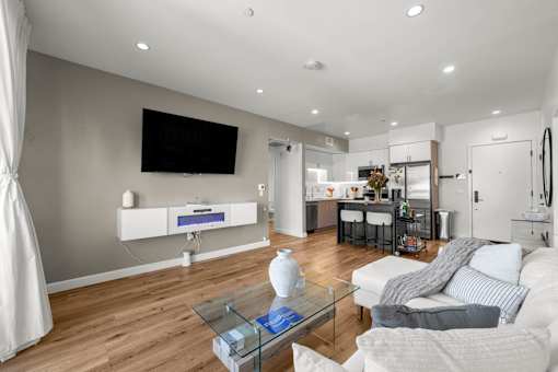 A modern living room with a white sofa, a glass coffee table, and a flat-screen TV mounted on the wall.