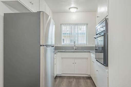 A kitchen with white cabinets and a grey refrigerator.