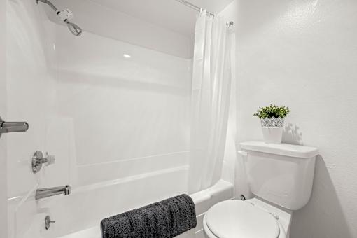 A white bathroom with a towel hanging on the tub.