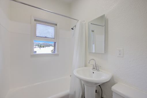 A white bathroom with a sink, mirror, and tub.